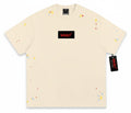 VaultWear cream cotton crewneck t-shirt featuring a black logo patch with red text and multi-colored paint splatters.